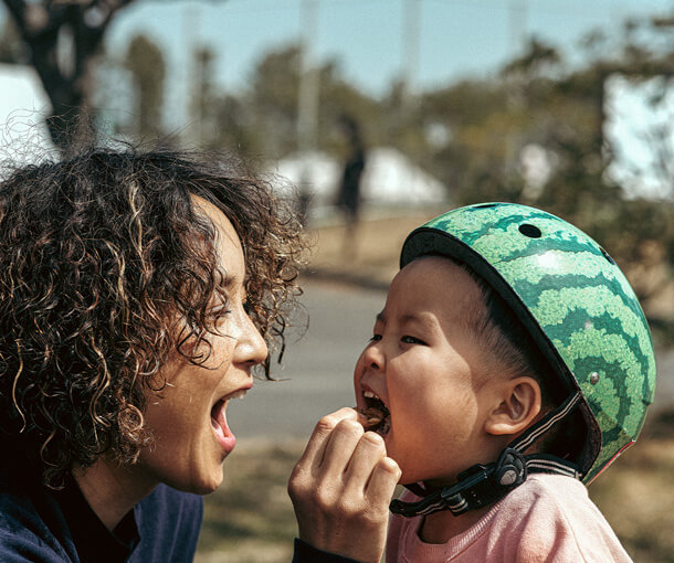 A mum feeds vitamin D rich food to a child wearing a bicycle helmet
