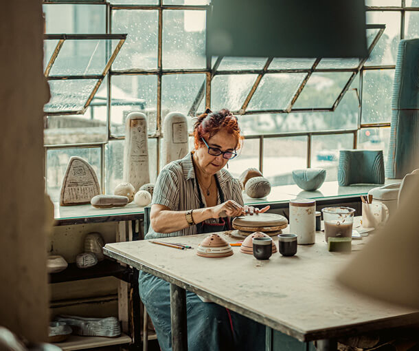 A woman crafts clay pottery at a table on a rainy day
