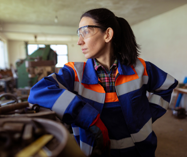 A woman in a construction trade leans against her tools and looks out the window