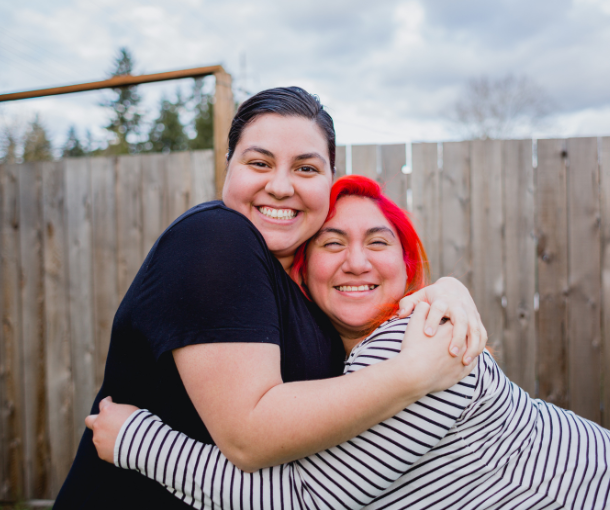 Two women embrace each other and are smiling at the camera